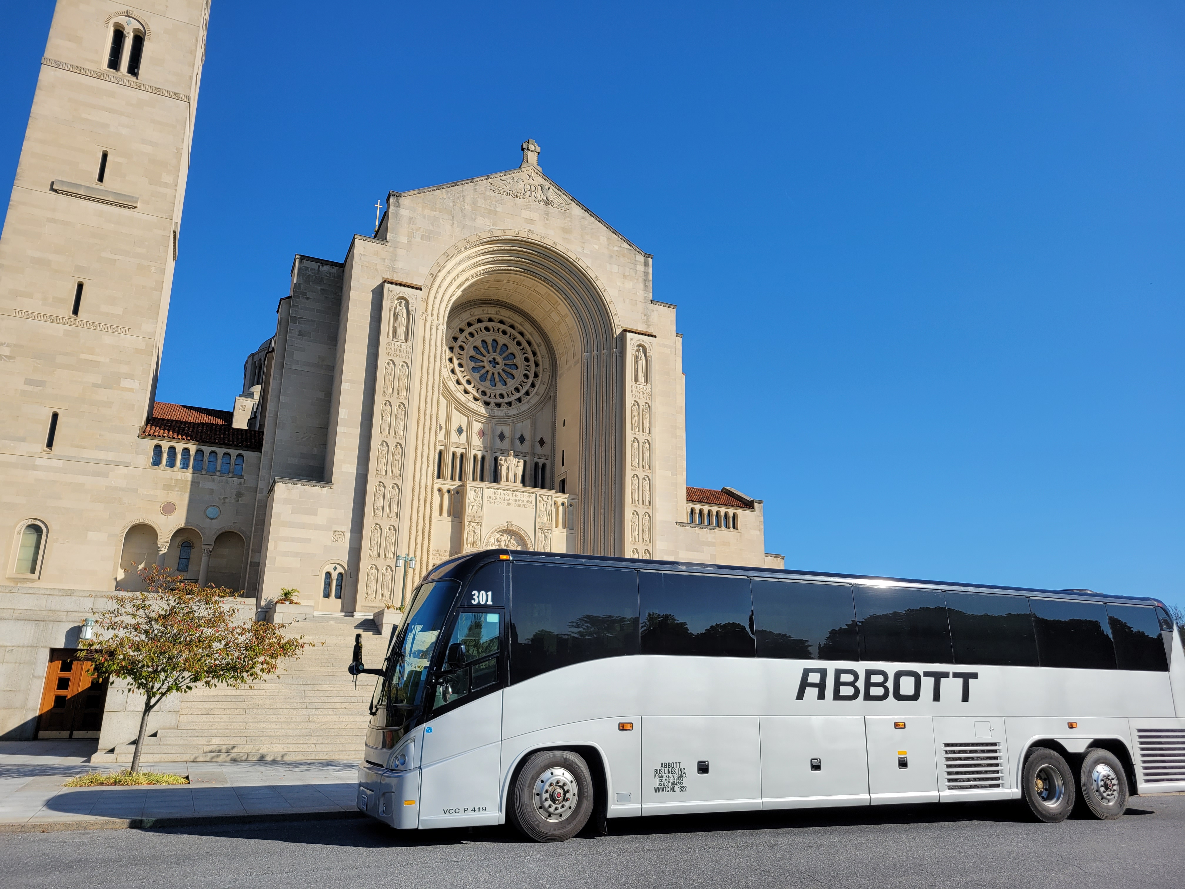 A motorcoach, Abbott Bus on the road that meets a sidewalk with a church behind it